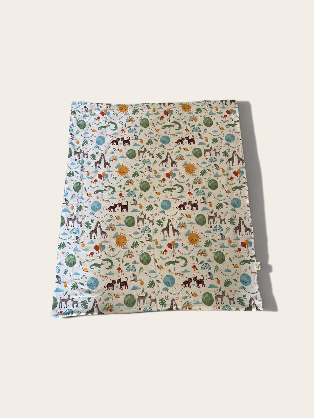 a blanket or pouch, featuring a whimsical safari animal print on a cream background with blue, green, orange, and brown illustrations, shown on a light beige background.