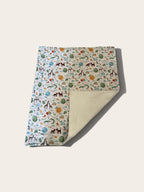 A folded blanket with a whimsical safari-themed print on one side and a soft cream fleece backing on the other, displayed on a light beige background.