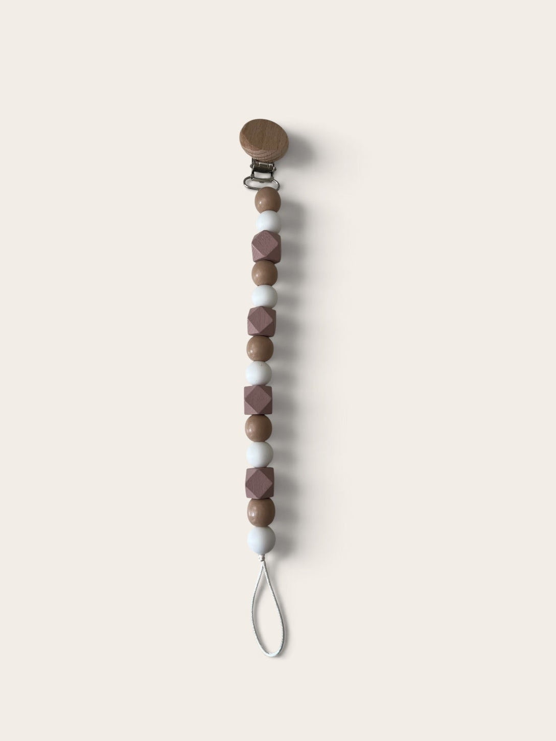 A pacifier clip with a wooden spoon-style clasp, a vertical string of brown and mauve beads, and a white loop at the bottom, shown on a solid light beige background.