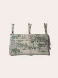 A cot organiser with a green safari toile pattern on a light beige linen-like fabric, featuring three adjustable tie straps at the top, shown against a solid off-white background.