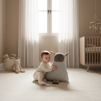 A baby in a cream onesie sits on a carpeted floor in a softly lit nursery, holding a large white plush sheep toy. 