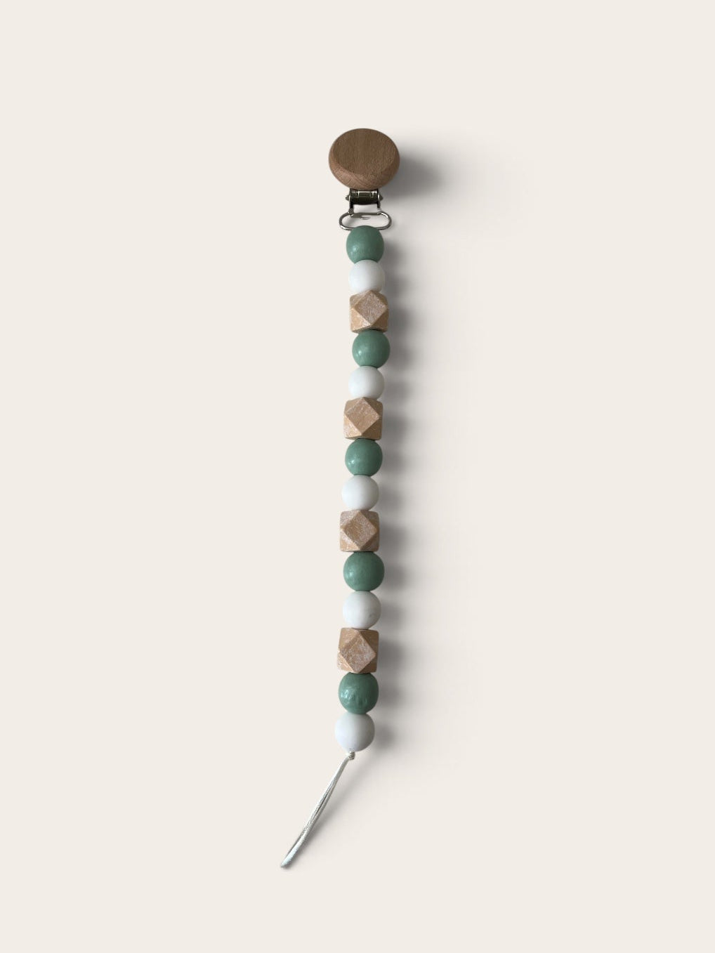 A wooden pacifier clip with a round brown wooden top, a silver metal clasp, and a dangling string of faceted wooden beads in sage green, light beige, and medium brown