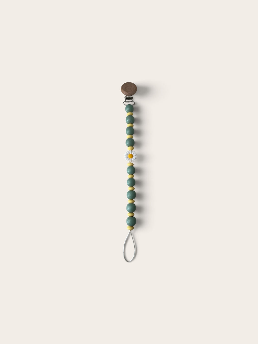 A beaded pacifier clip with sage green beads, small gold spacer beads, a white daisy accent, and a brown snap closure, shown on a solid light beige background.