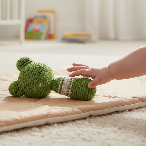 Baby reaching for crocheted frog rattle toy on play mat in nursery