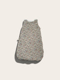 A sleeveless baby sleeping bag or pouch with a dense small floral print on a light beige background, featuring a white zipper at the top and a side zipper, shown against a solid off-white background.