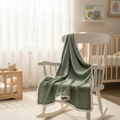 Green muslin baby blanket made from bamboo cotton draped over a nursery rocking chair.