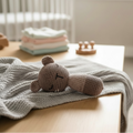 Knitted teddy bear baby comfort toy on blanket in neutral nursery setting