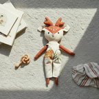 Soft reindeer heirloom doll lying on neutral rug with baby toys, blanket and warm sunlight
