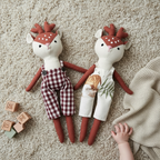 Two soft reindeer heirloom dolls lying on neutral rug with baby hand and wooden toy