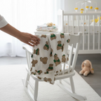 Teddy bear print muslin baby blanket made from bamboo cotton draped over a white rocking chair in a nursery.